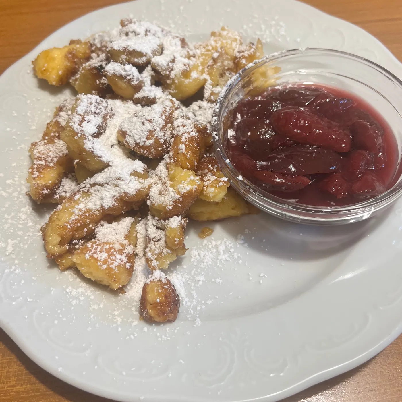 Kaiserschmarrn mit Staubzucker, daneben ein Glasschälchen Röster, auf einem weißen Teller