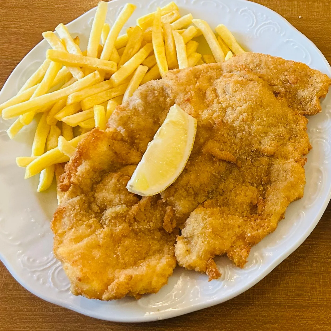 Schnitzel mit Pommes frites und einer Zitronenspalte auf einem weißen Teller, fotografiert von einem Gast